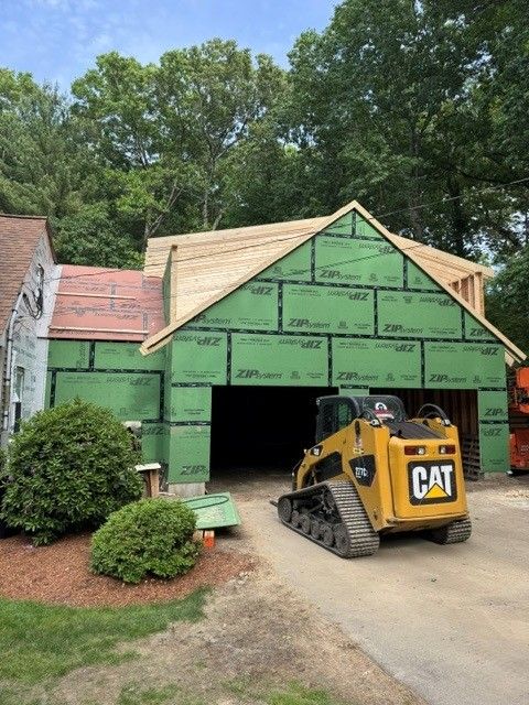 Yellow CAT skid steer in front of a green house under construction with exposed roof and garage opening