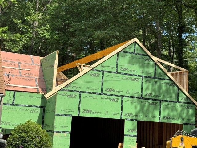 Partially built house with green sheathing and a gabled roof under construction in a wooded area