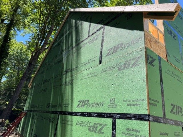 House under construction wrapped in green ZIP System sheathing in a wooded area