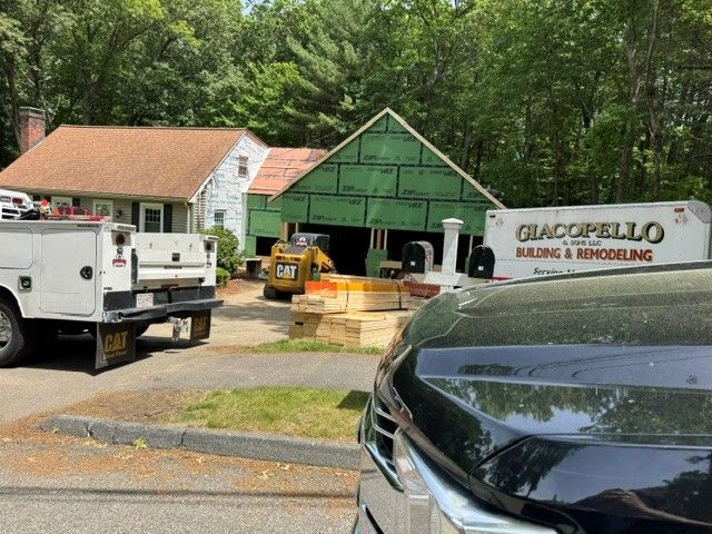 Construction trucks and materials outside a green house under renovation, with a white work truck in front.