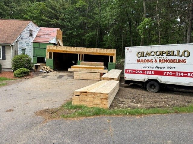 Construction site beside a house with lumber stacked near a trailer and a partially built green structure