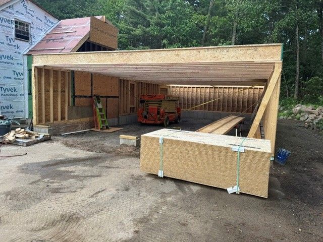 Partially built wooden garage with a red lift inside and a large panel leaning in front