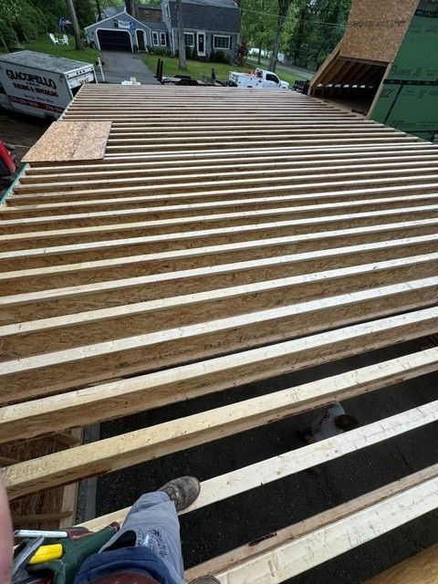 Roof deck under construction with exposed wooden joists and shingles, viewed from above
