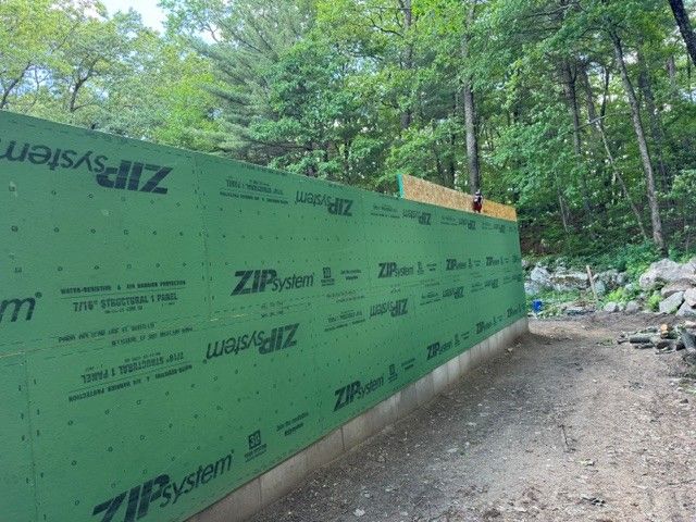 Green Zip System wall panels line a dirt path in a wooded construction area