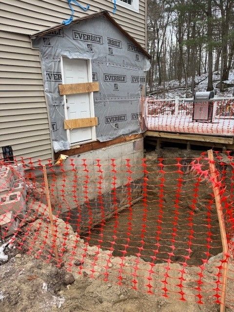 Exterior house under construction with a deep excavation, safety fencing, and a door.