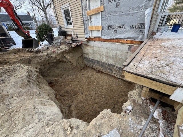Excavation next to a house with exposed foundation; dirt and snow visible.