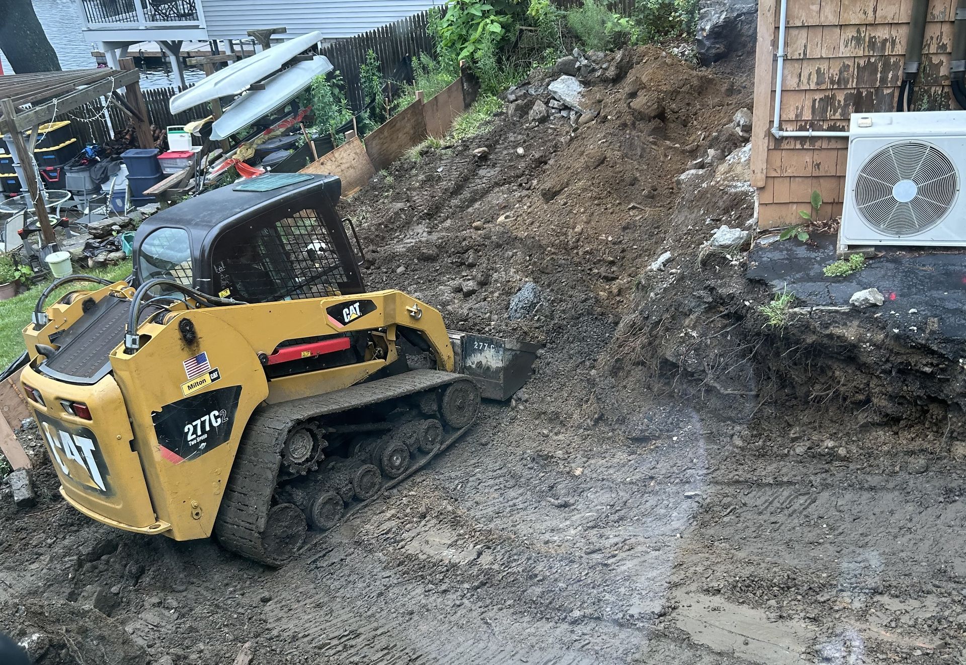 Yellow CAT skid steer removing mud and debris from a landslide near a building.