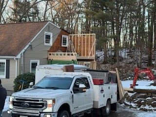 White work truck parked in front of a house under construction; a partially built wooden structure is visible.