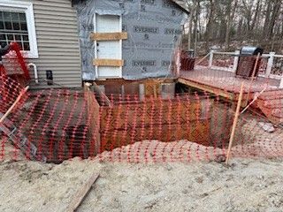 House exterior construction site; orange safety fencing surrounds an excavated area.