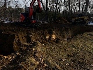 An excavator and bulldozer are digging a trench in a wooded area.