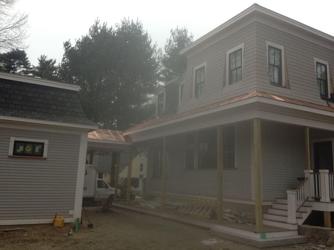 Two-story gray house with porch and connected garage under construction, overcast sky.