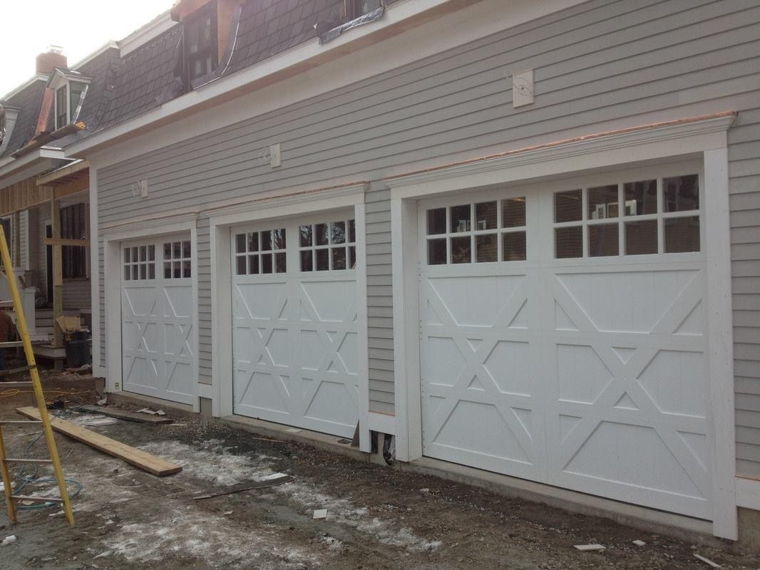 Three white garage doors with glass panels and decorative cross patterns on a light gray house.