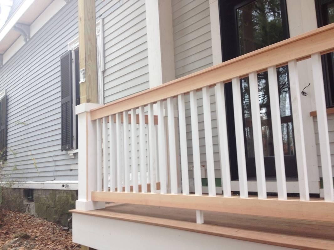 Newly constructed porch with white railings and wood trim on a light gray house.