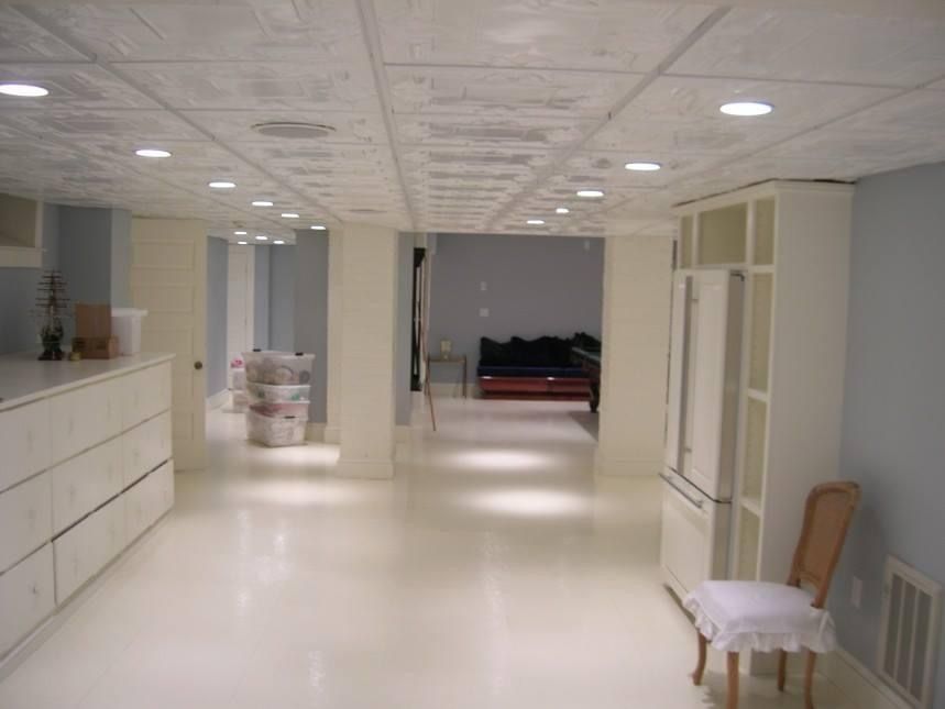 White basement room with recessed lighting, cabinets, and a tall refrigerator.