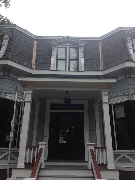 Victorian home with gray siding, copper roof trim, and a covered front porch with white columns.