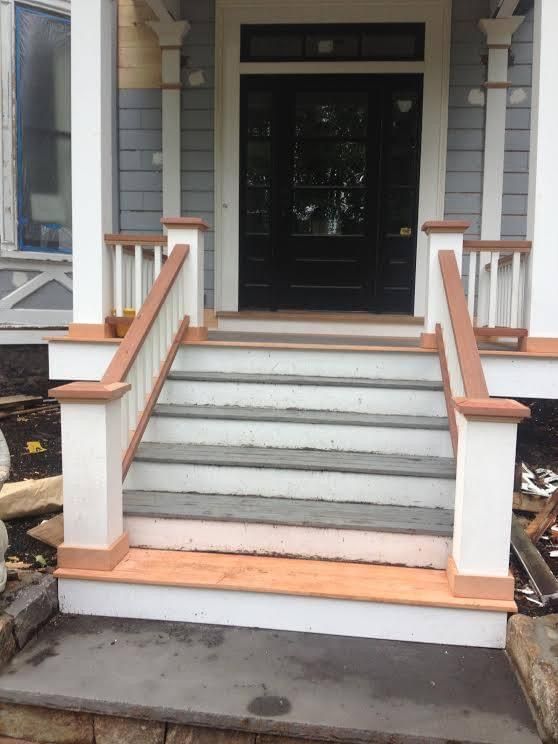 Entryway stairs with white and brown railing leading to a black door. Gray steps.