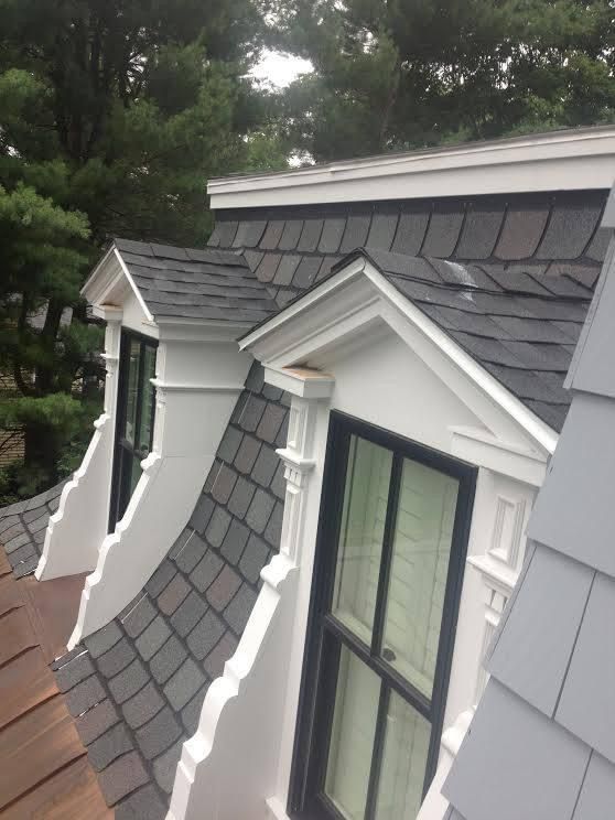 Dormer windows with dark gray shingles and white trim on a house roof.