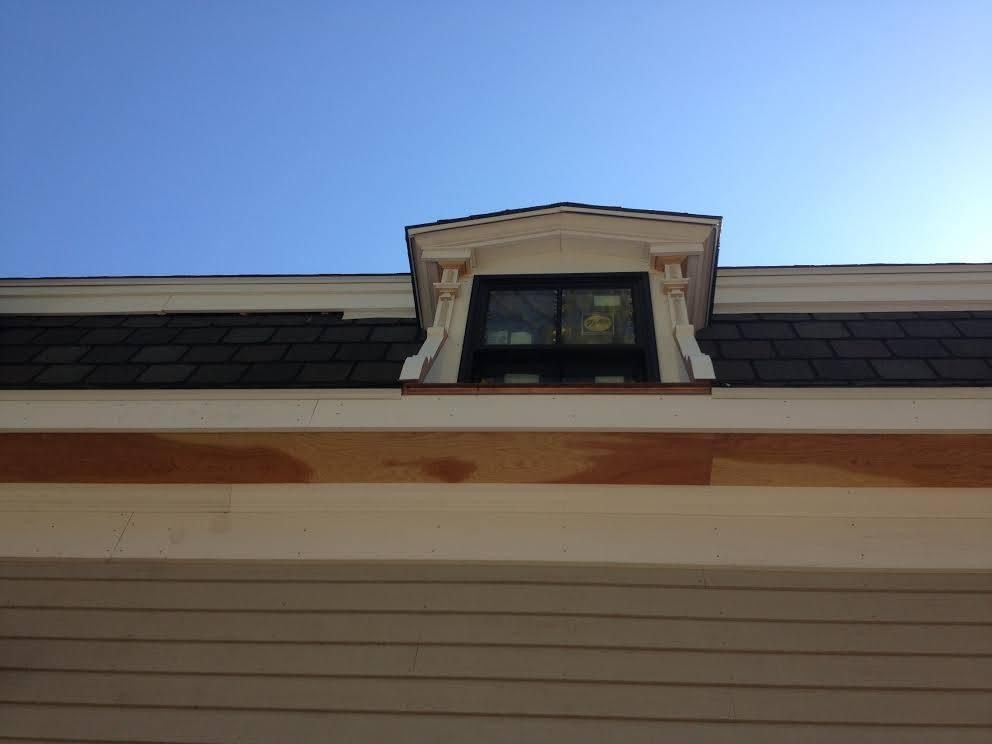 Dormer window on a house roof, against a blue sky.  The window has a decorative trim.