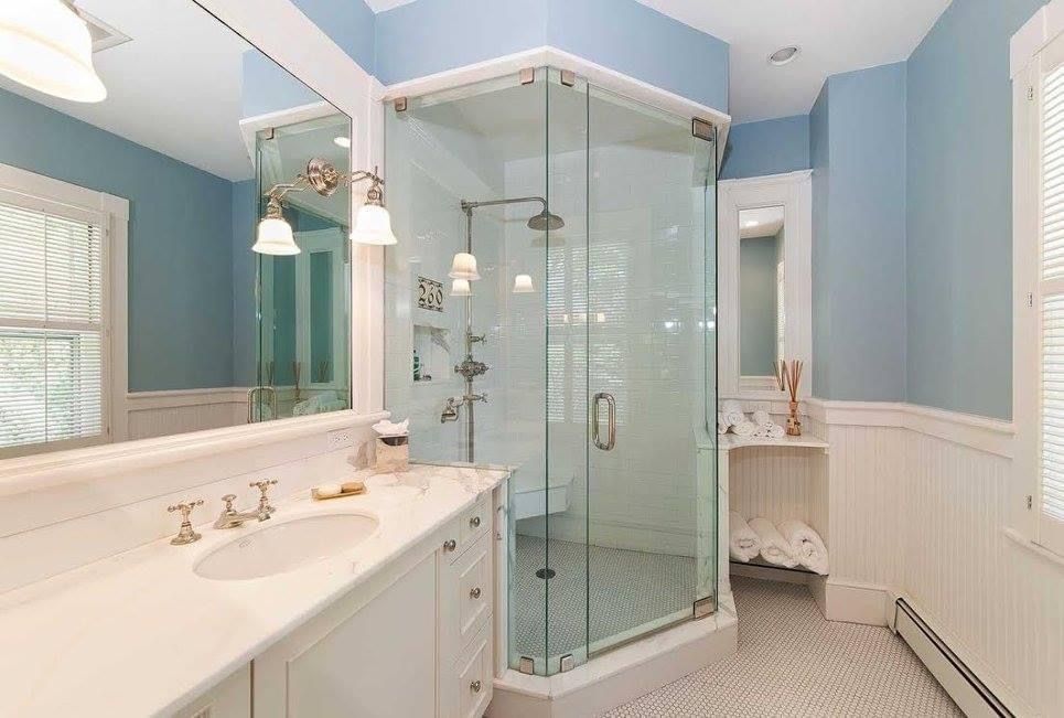 Bathroom with glass shower, white vanity, blue walls, and patterned tile floor.