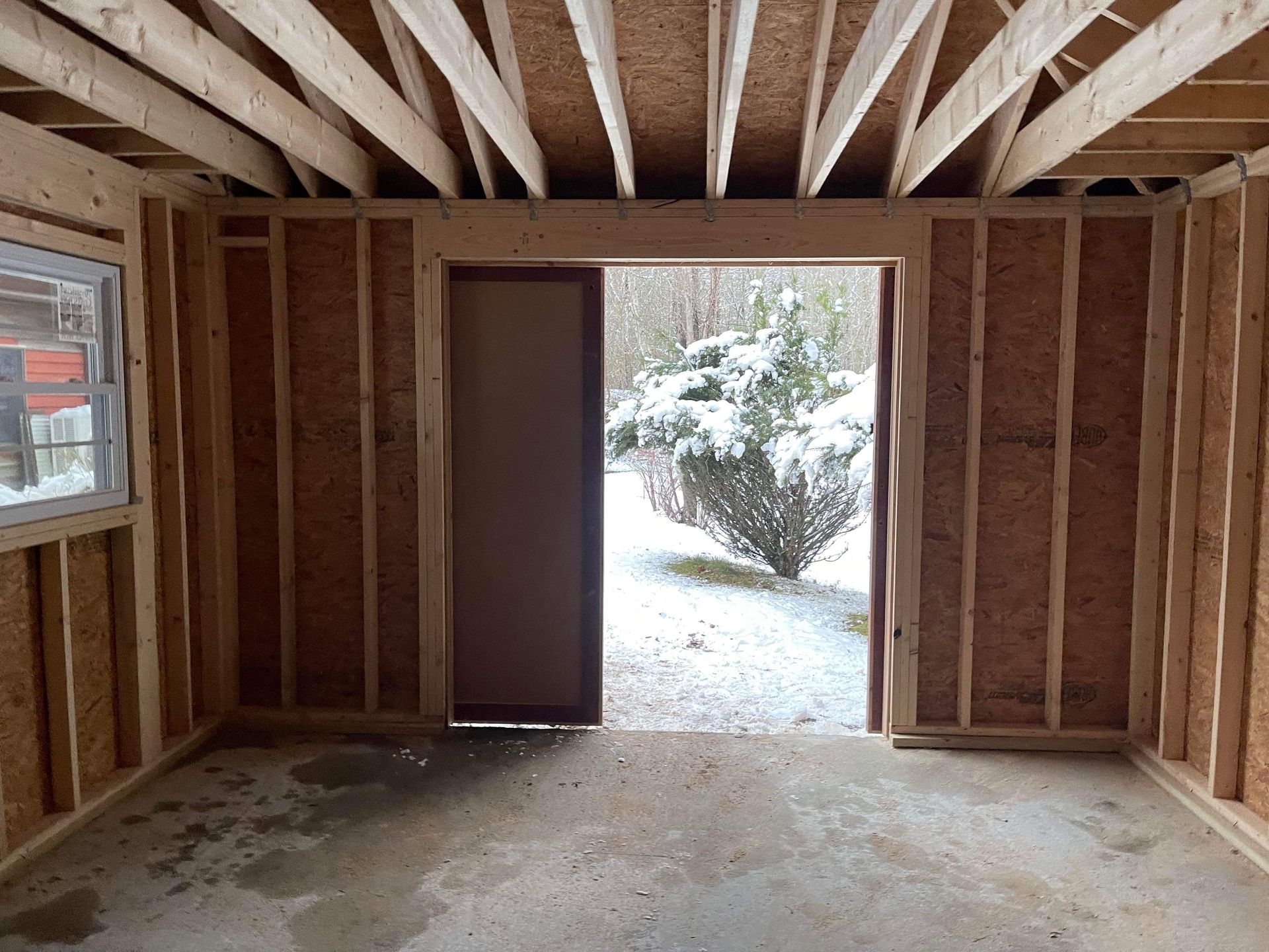 Interior of a wooden shed under construction, doorway open to snowy outdoors.