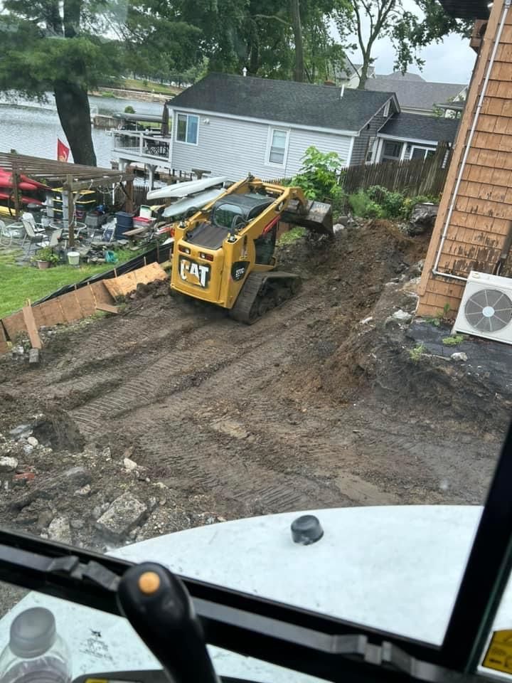 Yellow CAT skid steer on muddy hillside near houses and water.