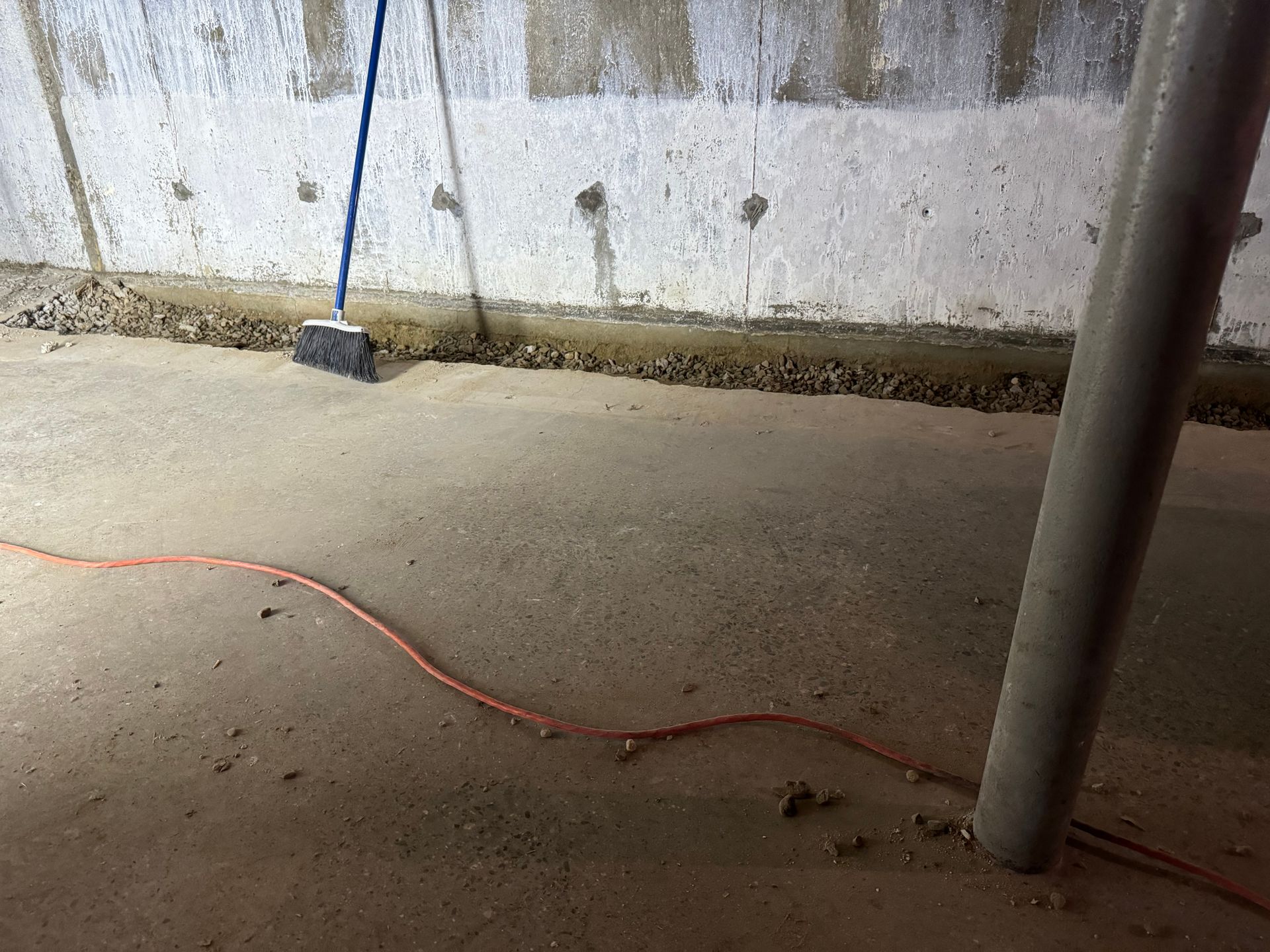 Concrete basement floor and wall with a broom, support column, and electrical cord.