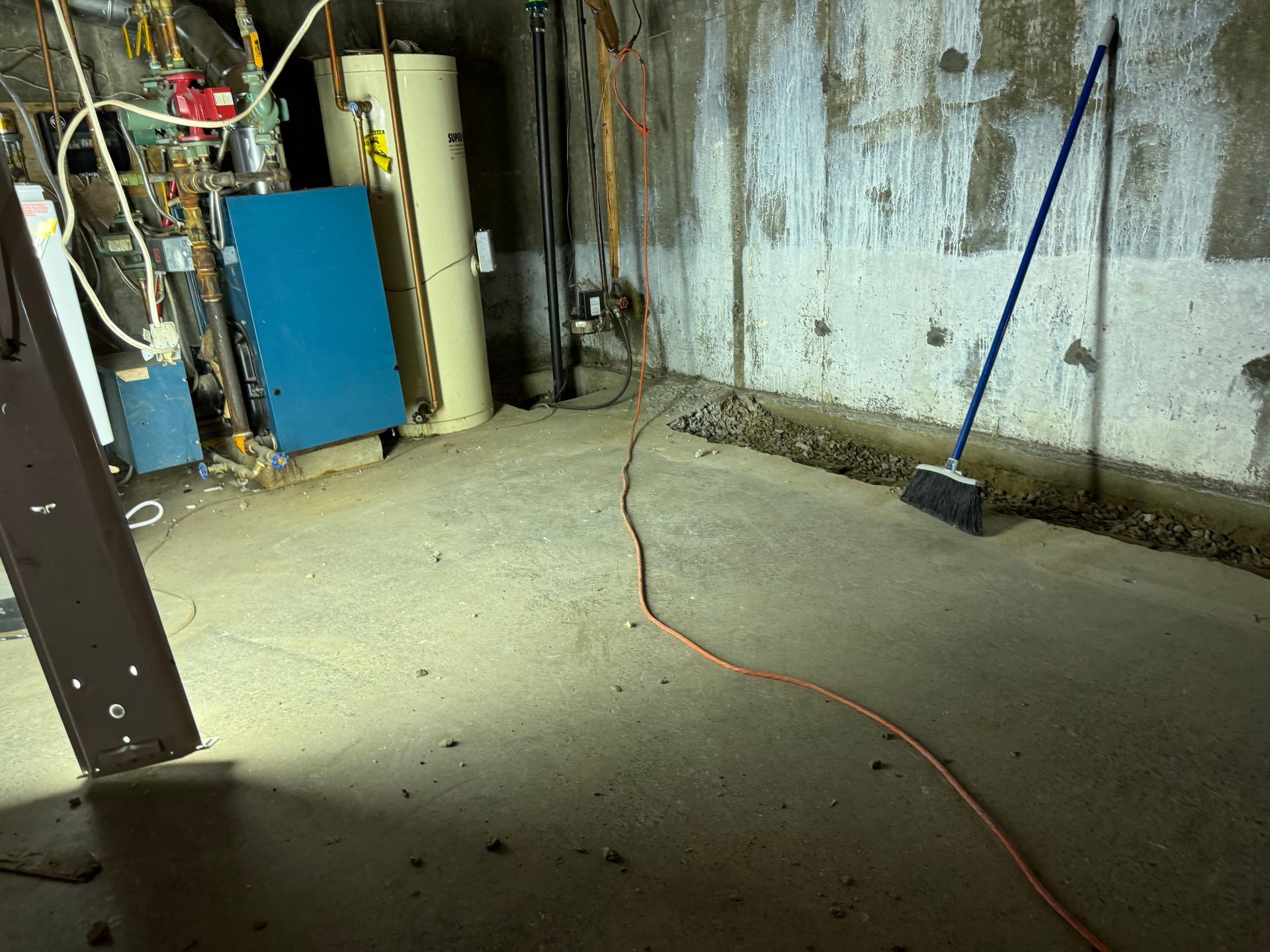 Concrete basement with utilities, extension cord, and broom.