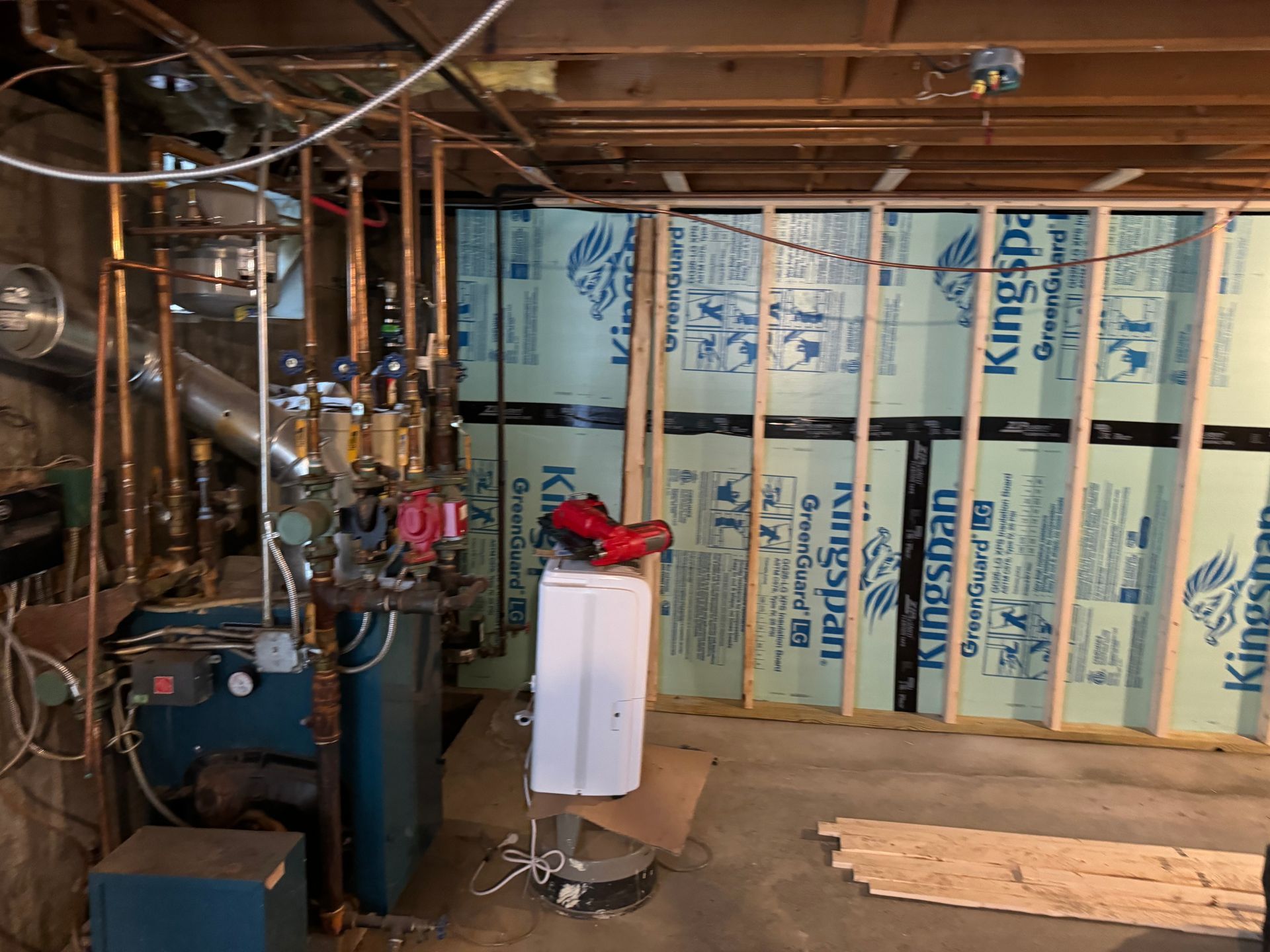 Basement with boiler, copper pipes, framing, and insulation. A small appliance sits on the floor.