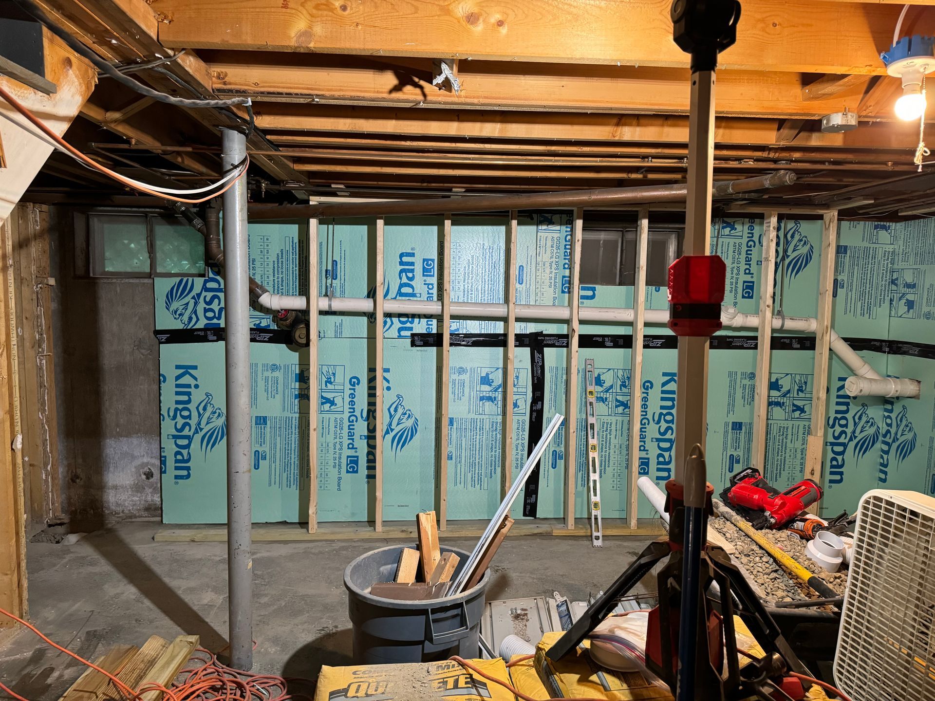 Basement framing with insulation, construction materials, and a work light.
