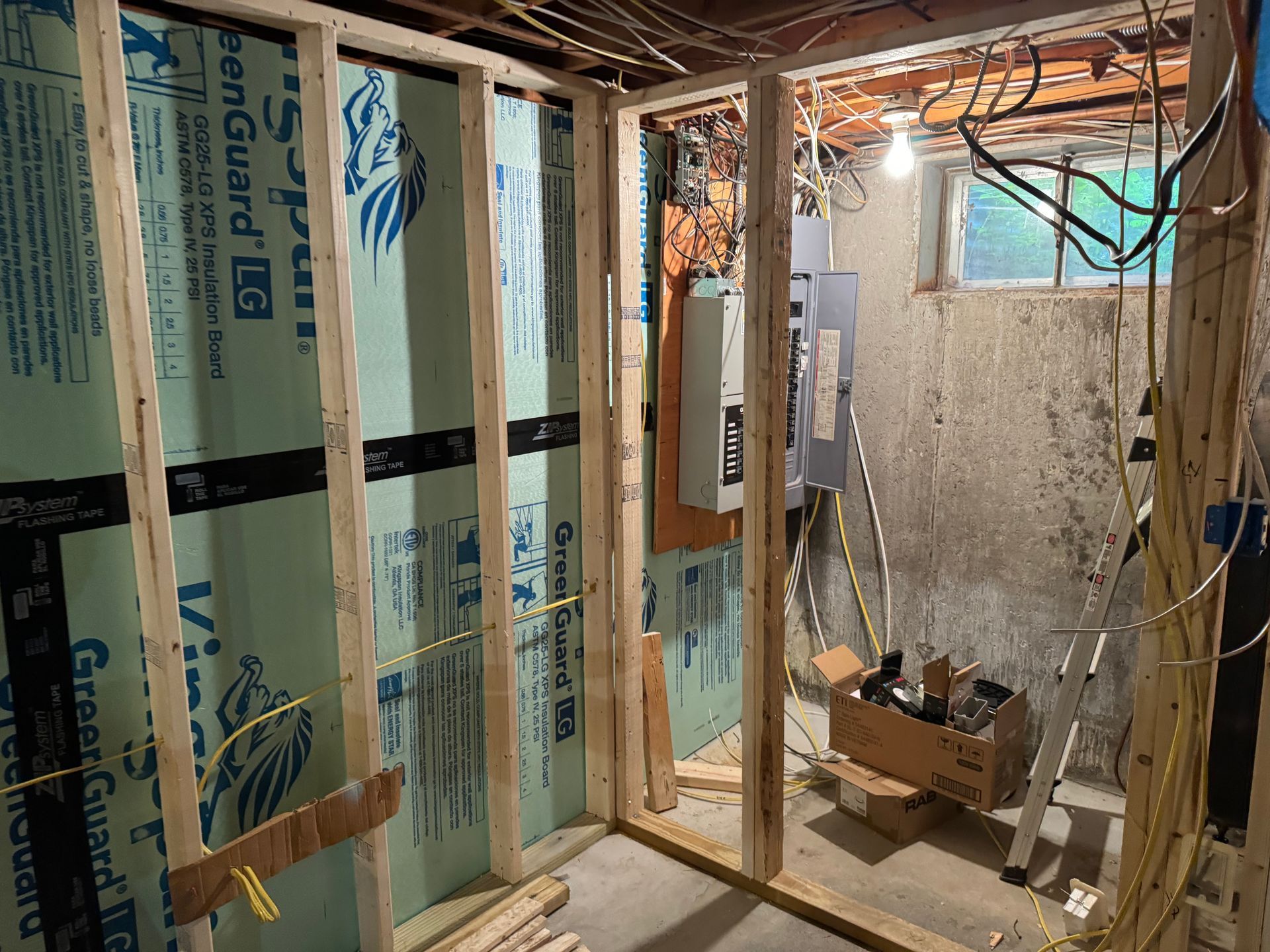 Basement room with new wooden frame construction, green insulation, electrical wiring, and unfinished concrete walls.