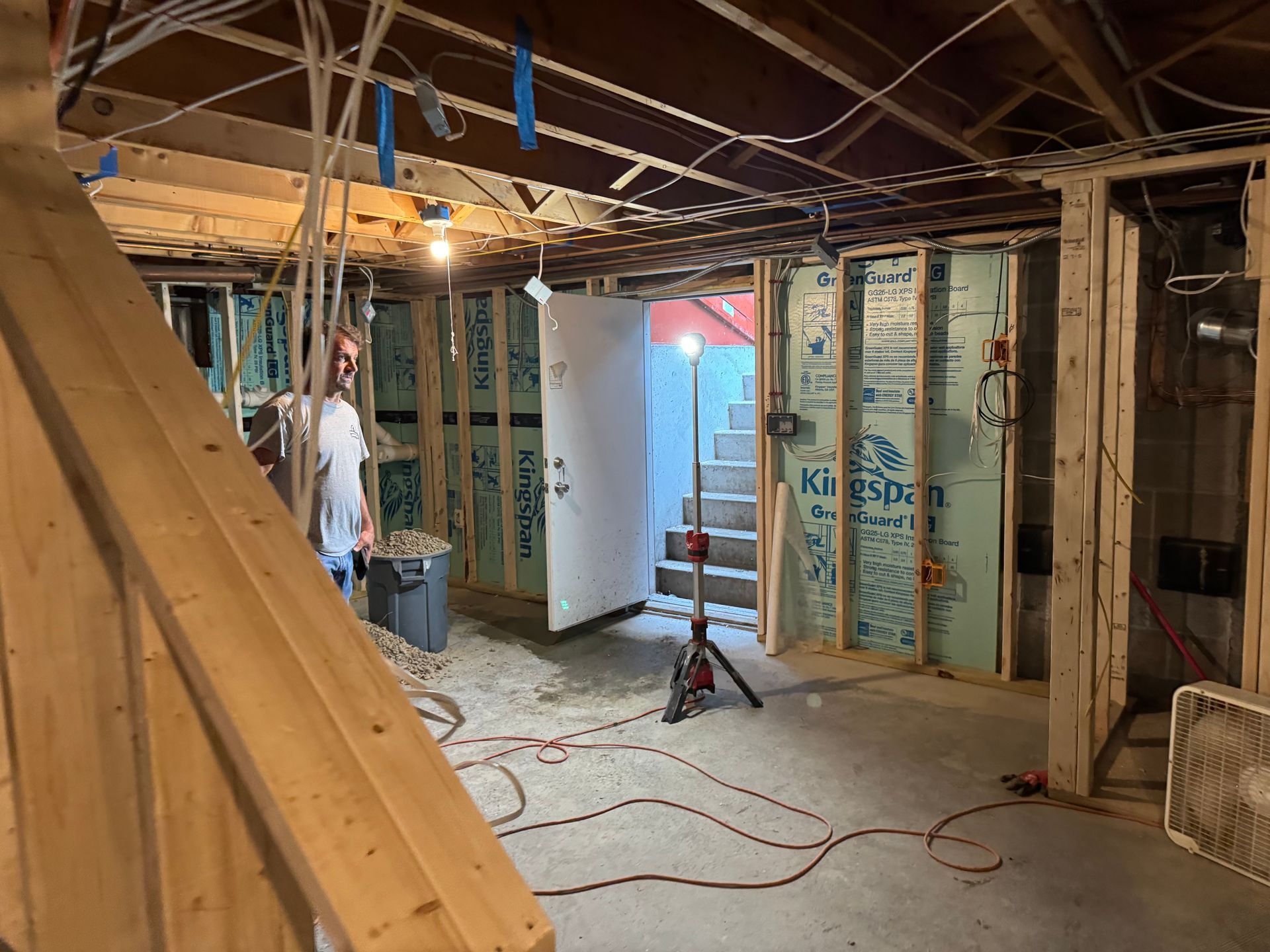 Basement renovation in progress; unfinished walls, exposed wiring, open doorway, stairs, and a worker.