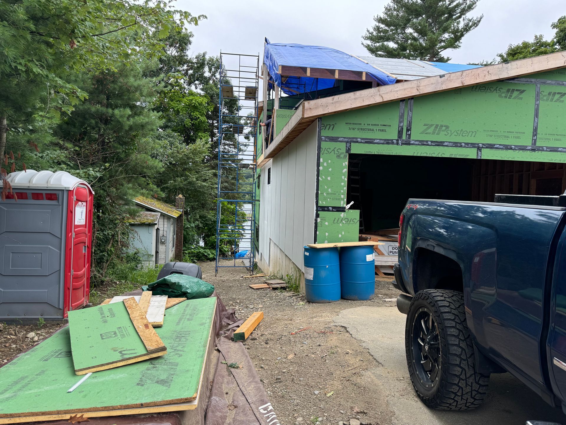Construction site with blue tarp, scaffolding, and porta-potty next to a truck.