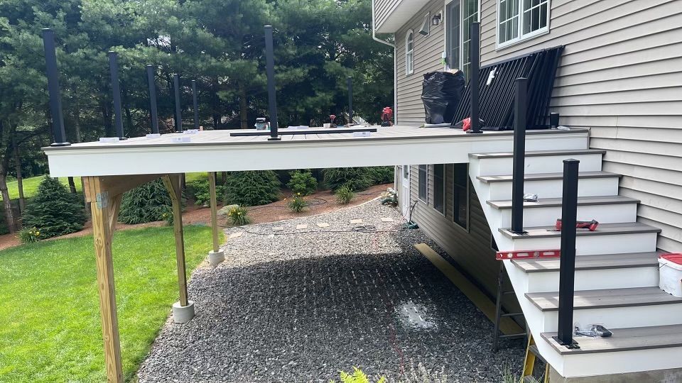 Deck construction: Elevated deck with stairs, black railings, gravel base, and a house.