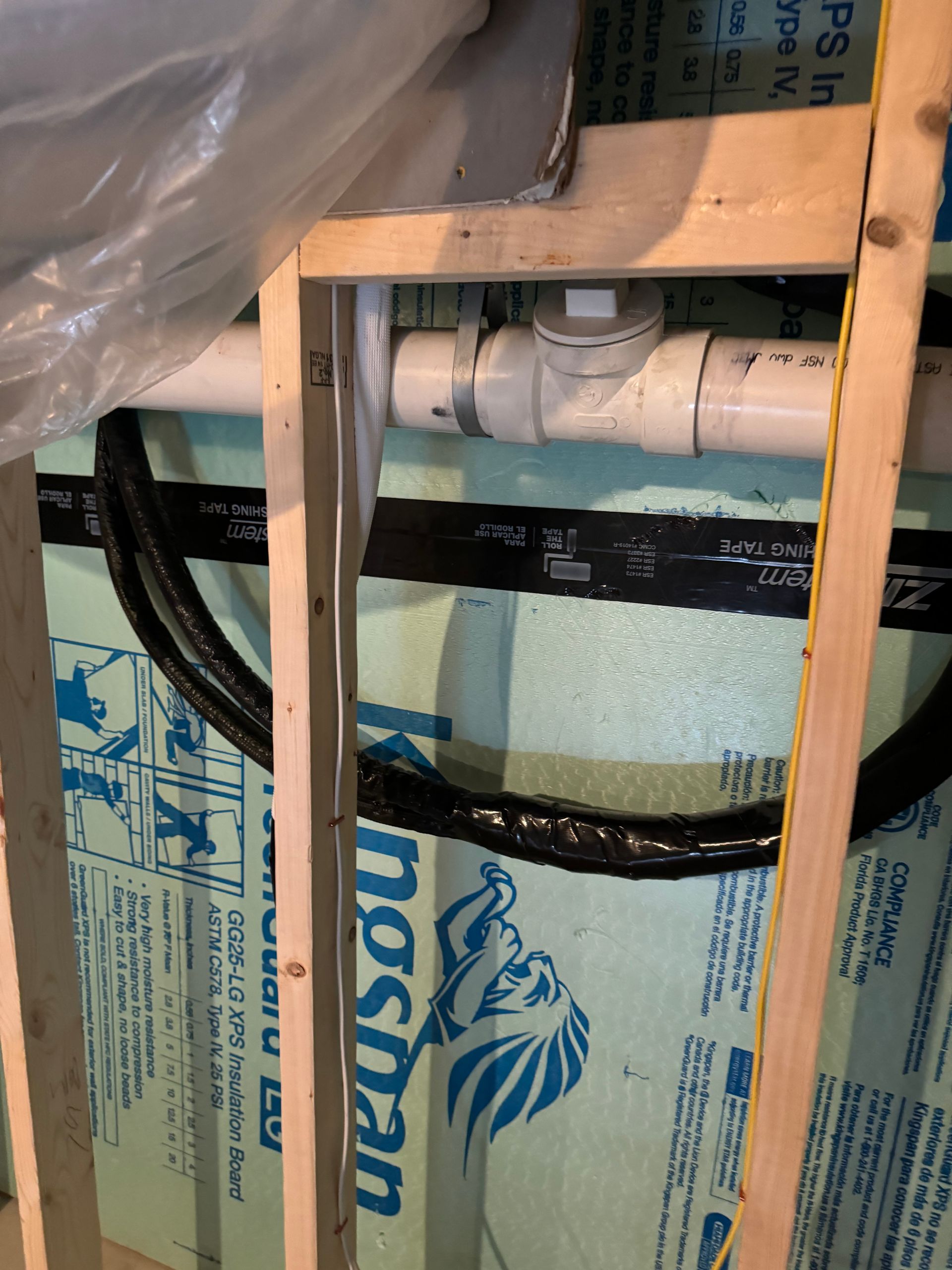 Framing around pipes in a wall cavity, with black cables and blue insulation visible.