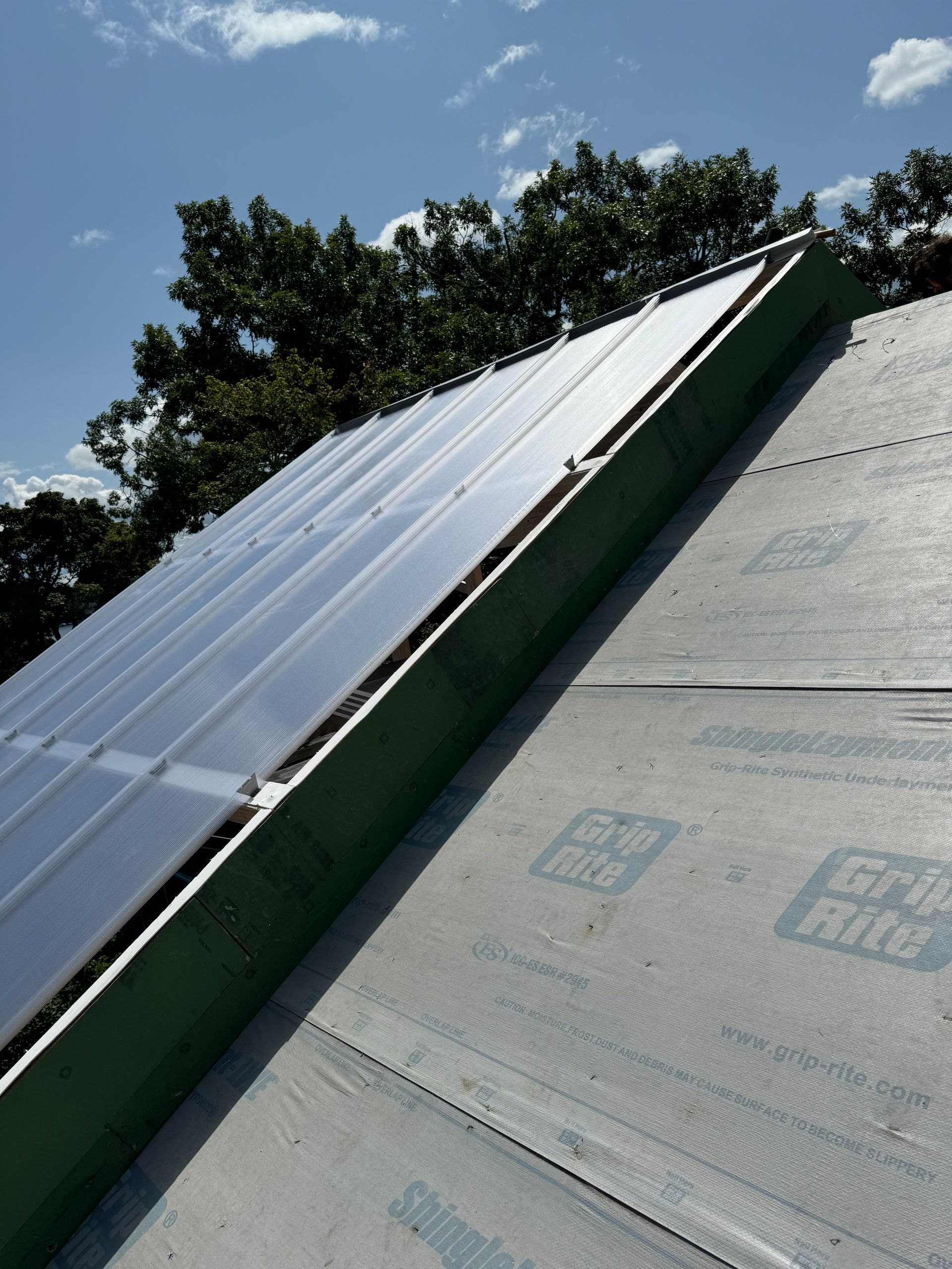 Solar panels on a sloped roof against a blue sky, with trees visible in the background.