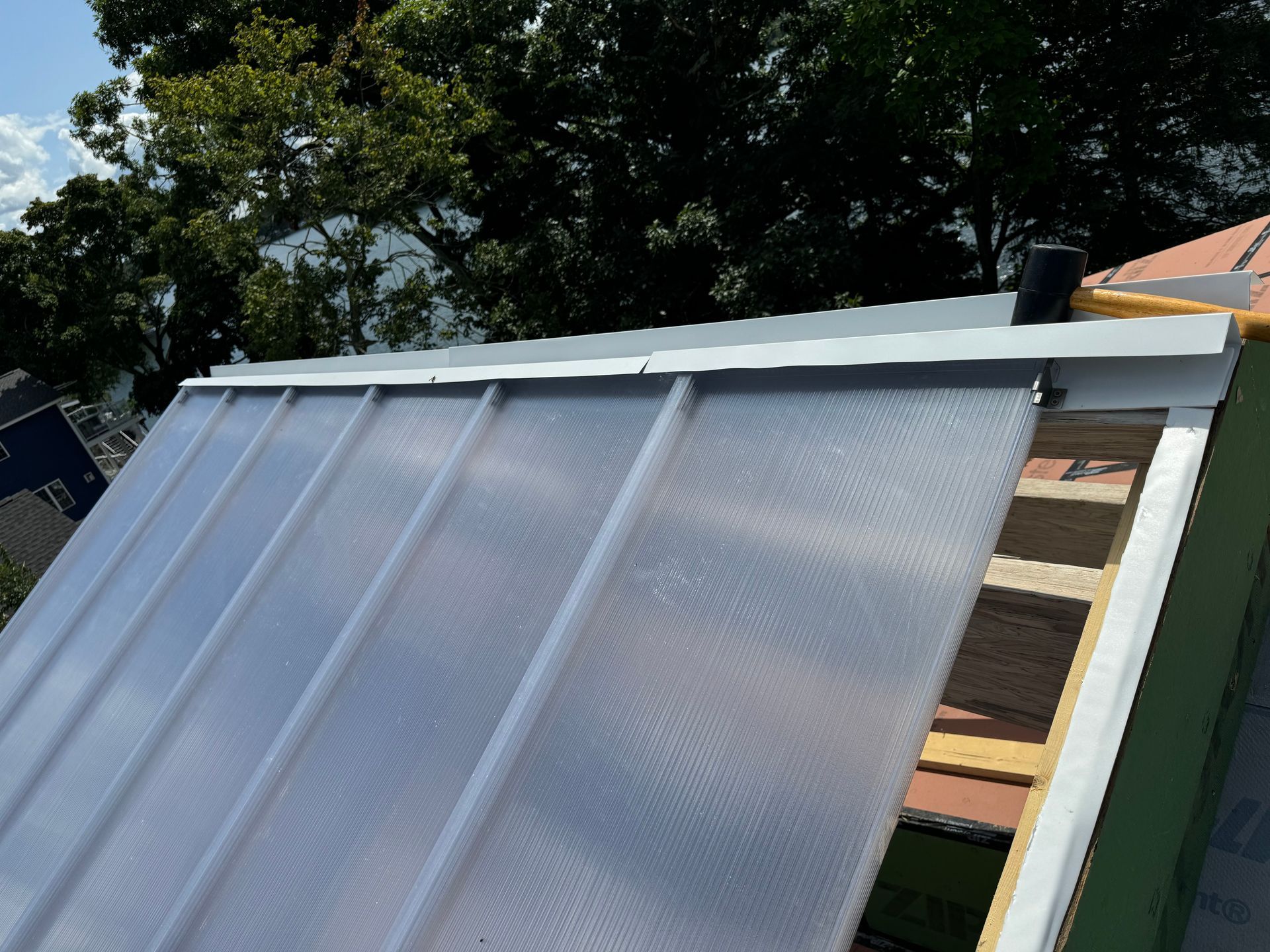 A metal and plastic roof with a tree-lined backdrop on a sunny day.