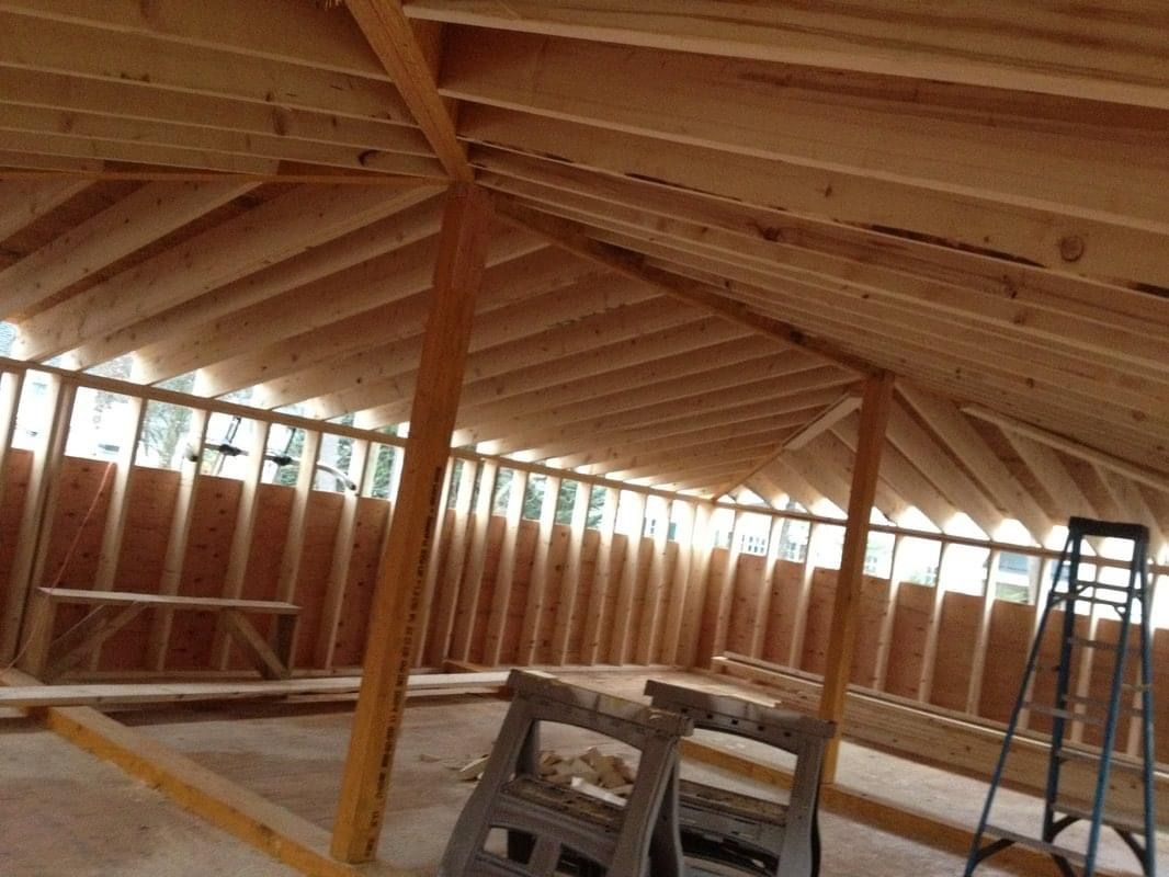 Interior view of a building under construction, showing wooden framing for walls and sloped ceiling.