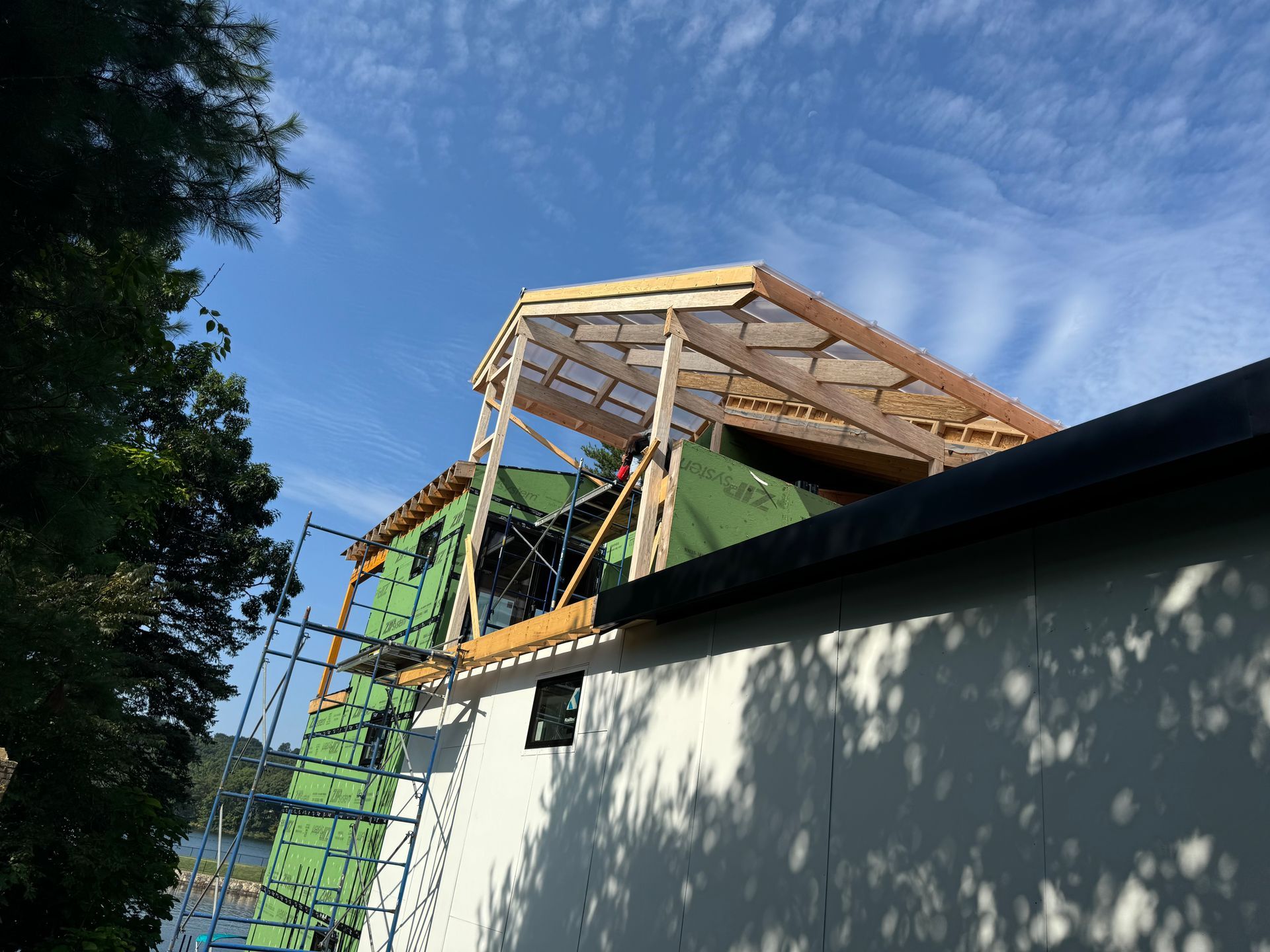 Building roof construction in progress; wooden frame on existing structure, blue sky in background.