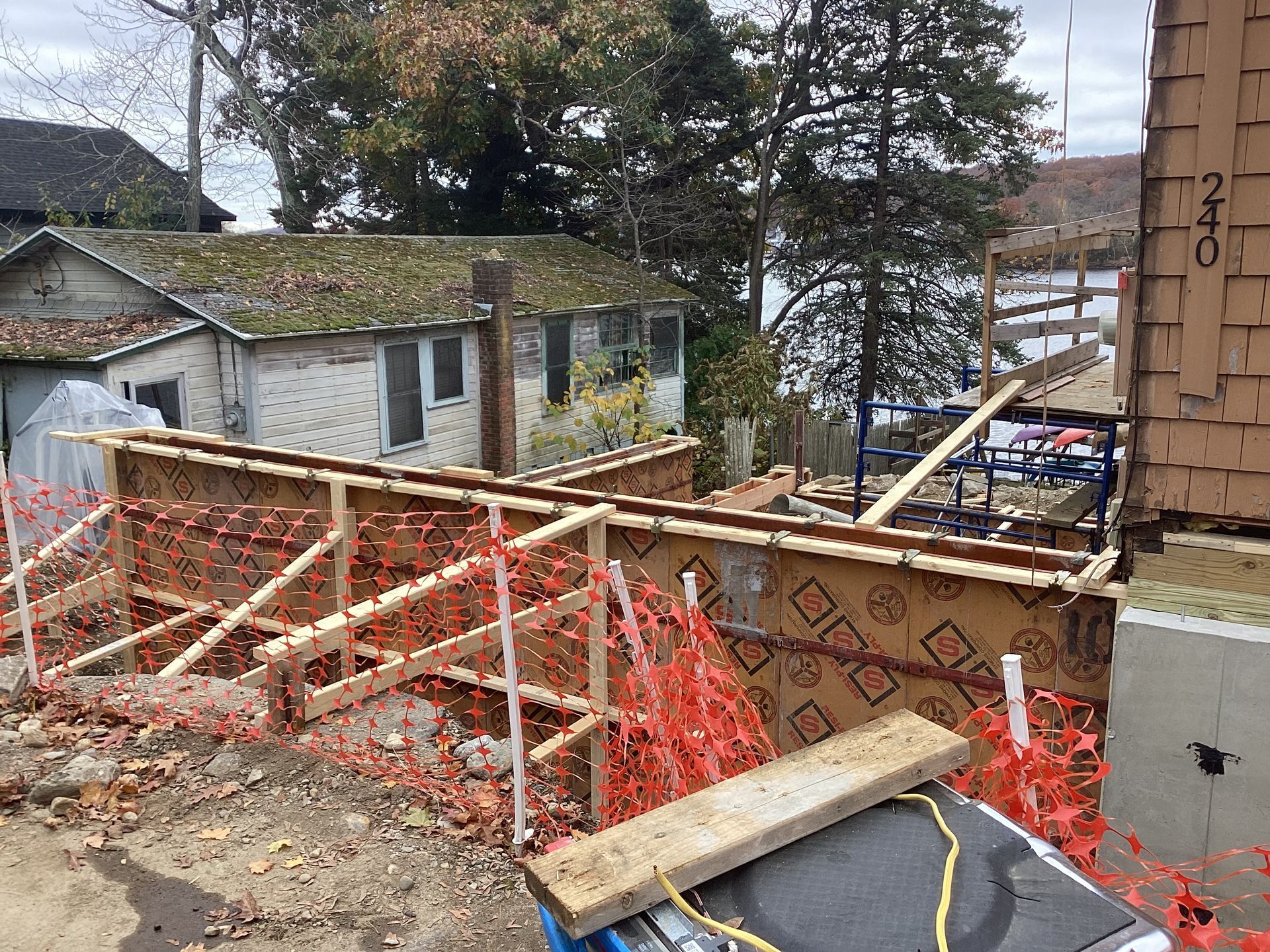 Construction site with wooden forms and safety fencing near waterfront buildings.