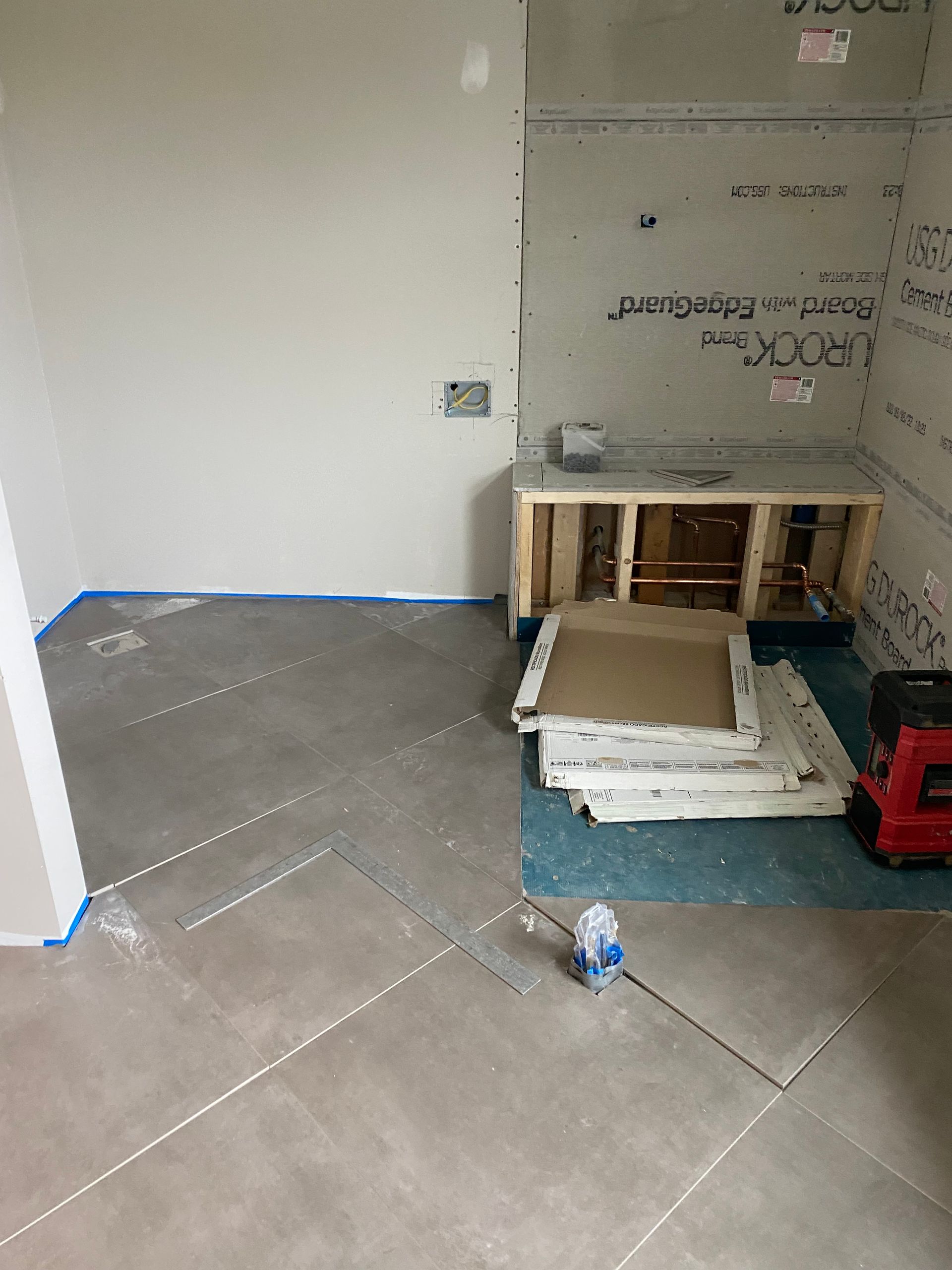 Bathroom renovation: grey tiled floor, framed bench, green waterproof barrier, and drywall.