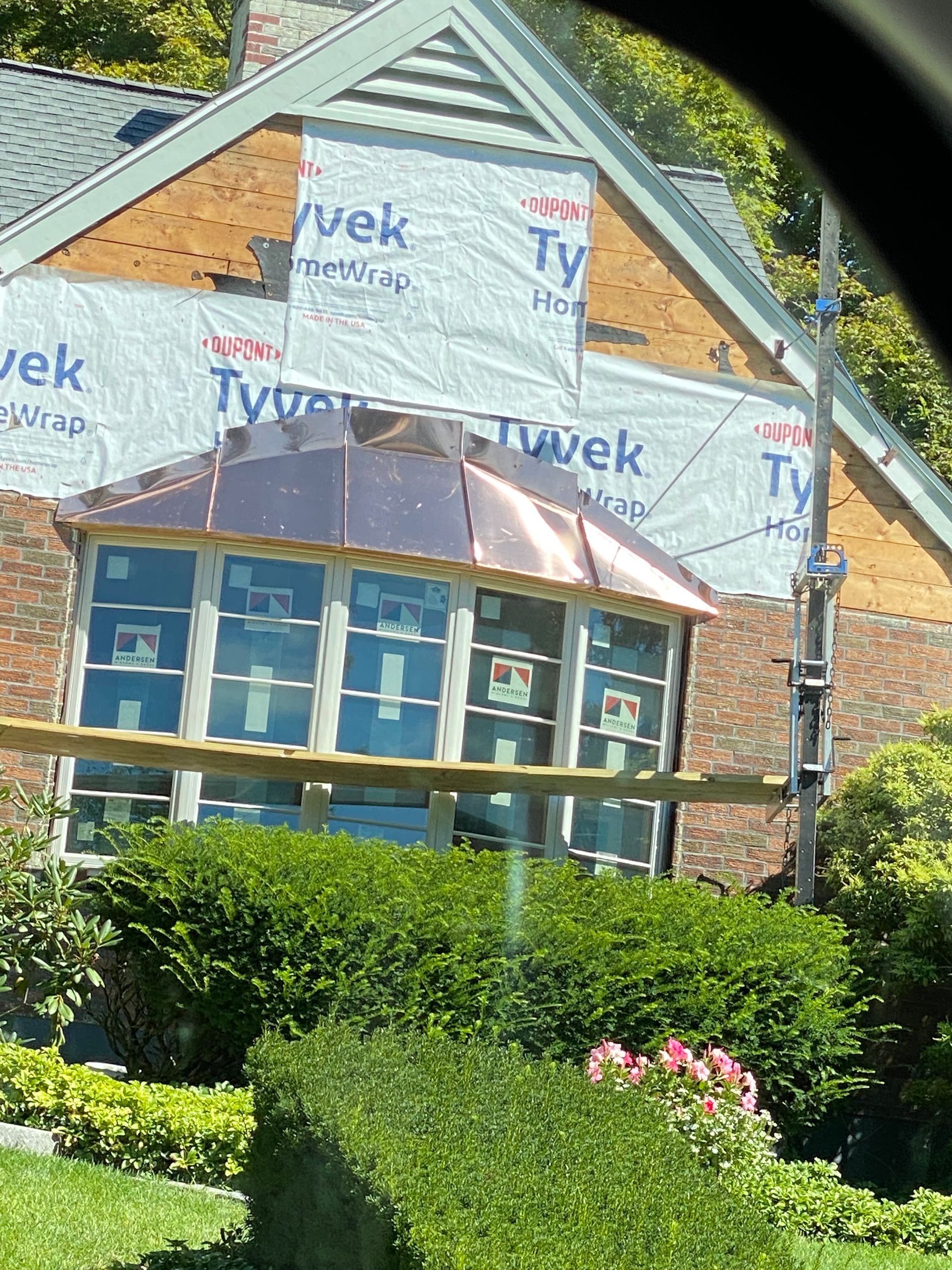 Copper-roofed sunroom with many windows under construction; scaffolding, brick wall, and Tyvek wrap visible.