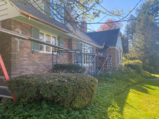 House with scaffolding, brick exterior, green shutters, lawn and shrubbery.