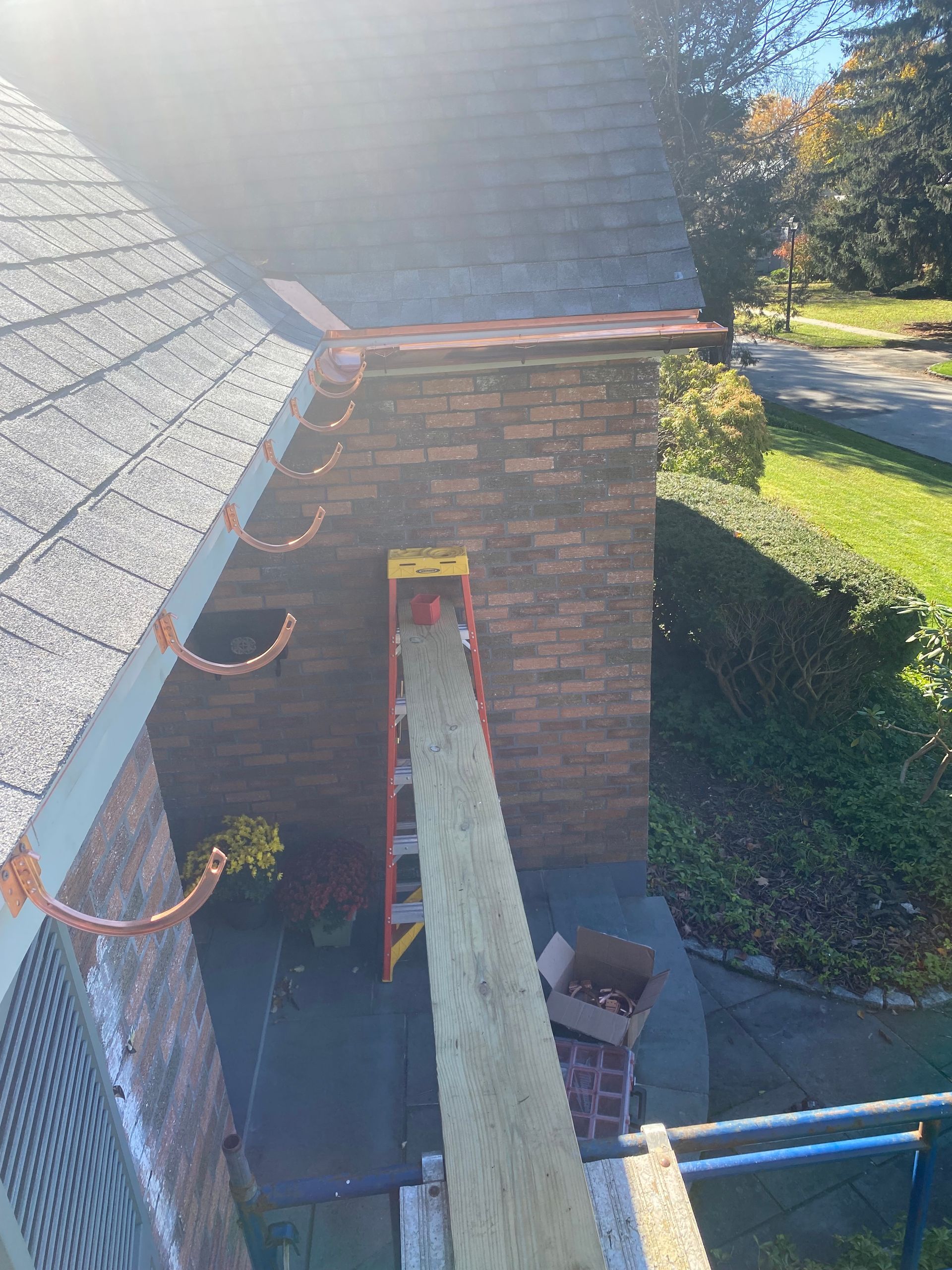 Ladder against a brick building, supporting a wooden plank. Copper gutters along roof.
