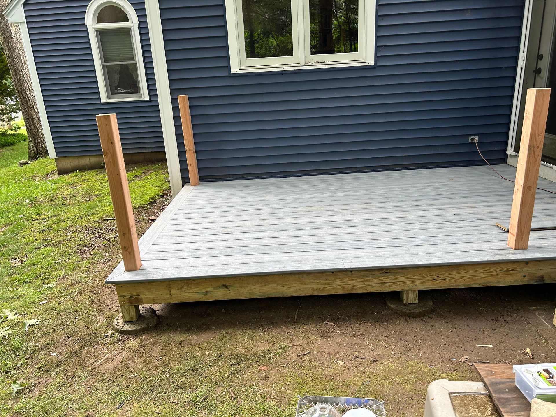 Wooden deck with posts against a blue house; on grassy ground.