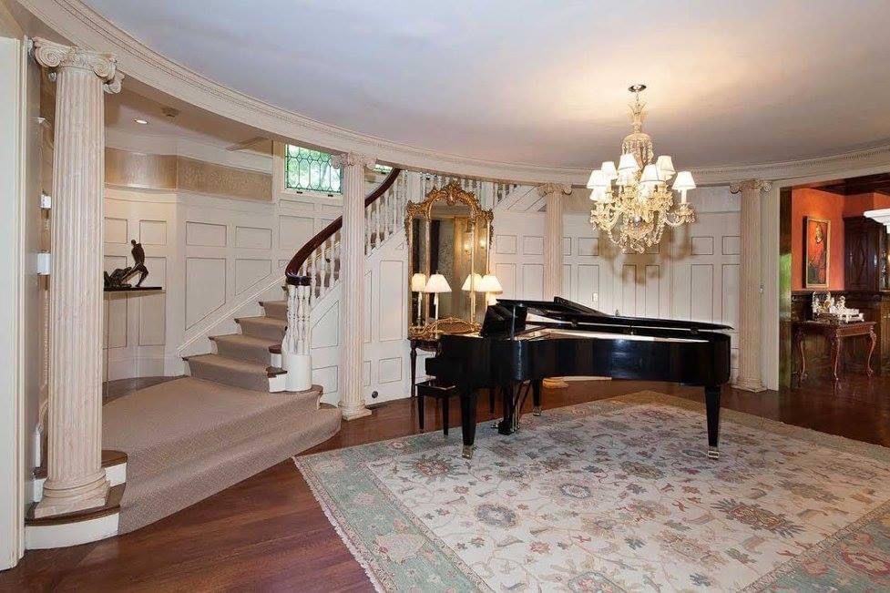 Elegant foyer with grand piano, chandelier, and curved staircase.