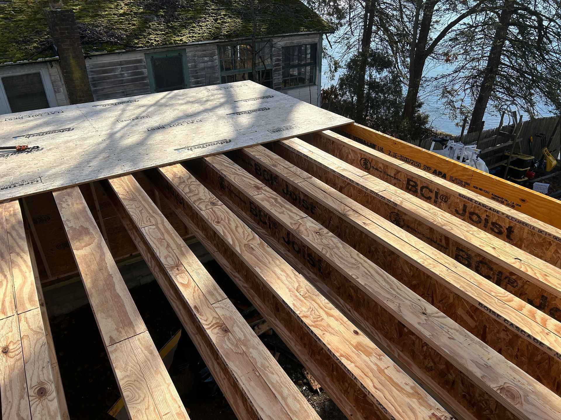 Wooden roof under construction; plywood over exposed joists; sunny outdoor setting.