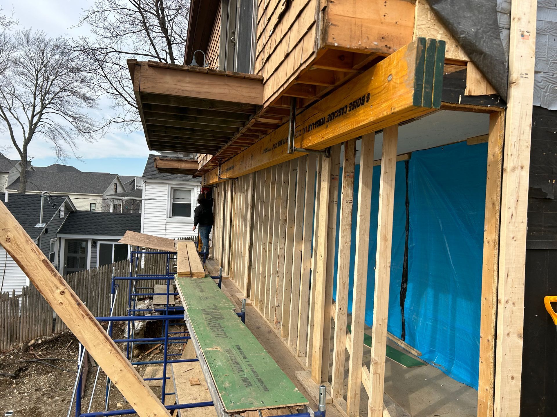 Construction in progress; wooden framing and scaffolding outside a building. Blue tarp visible.