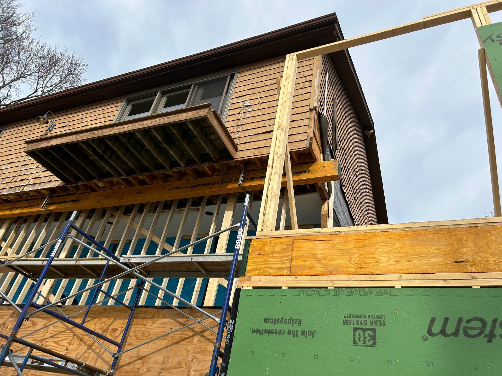 Construction site with a partially built wooden deck attached to a brown house. Scaffolding is visible.