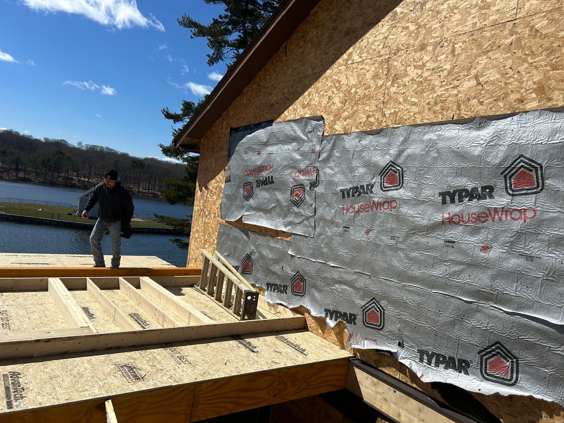 Construction worker on a roof with Typar house wrap visible; building in progress near water on a sunny day.