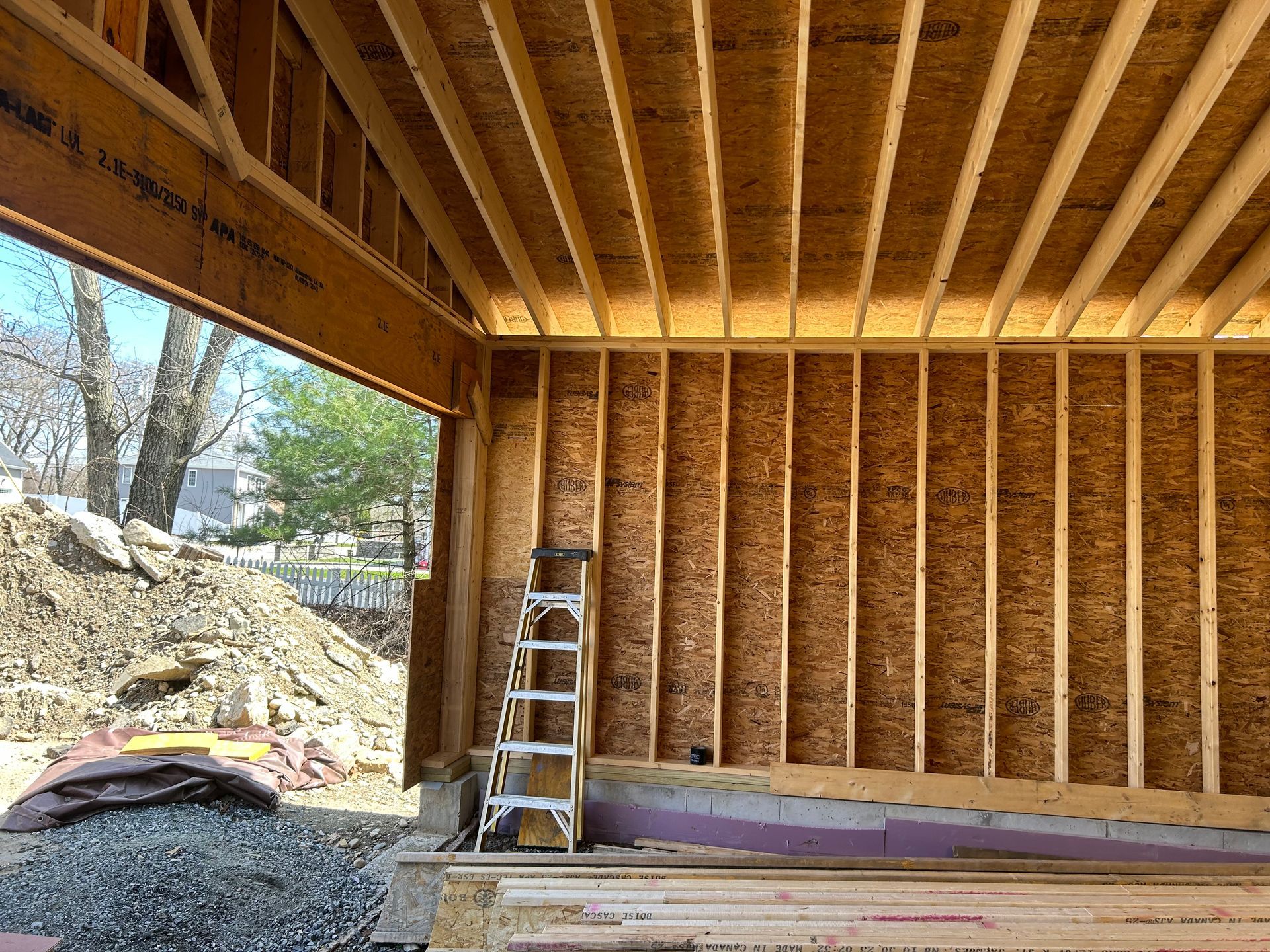 Interior of a building under construction, wooden framework visible. A ladder stands against a wall, exterior view.